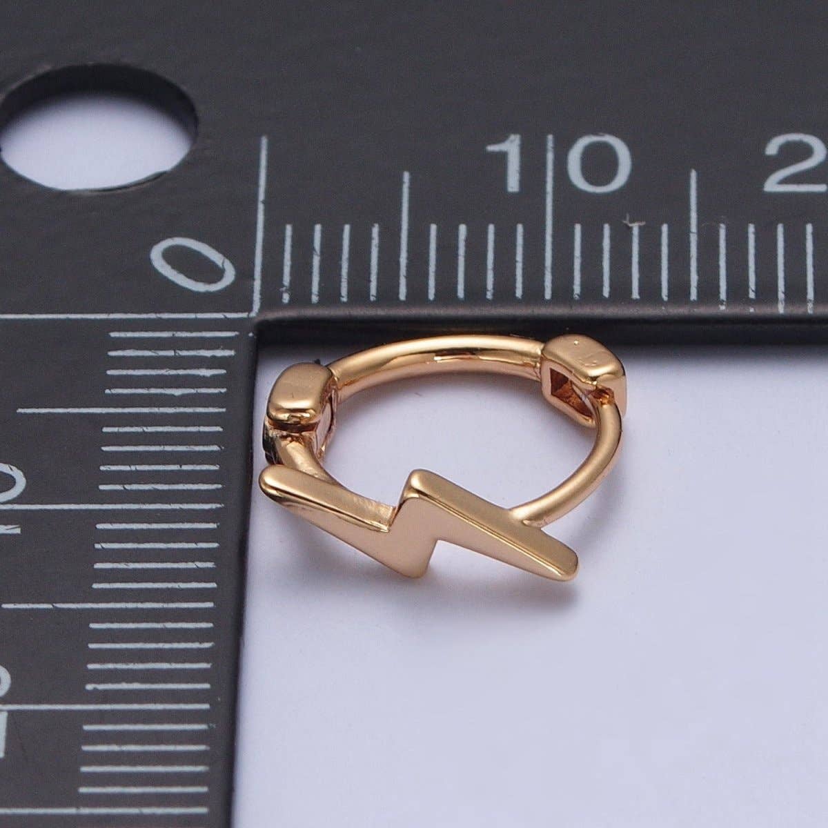 Gold lightning bolt huggie earring next to ruler showing 11.9mm size – dainty women's hoop earring
