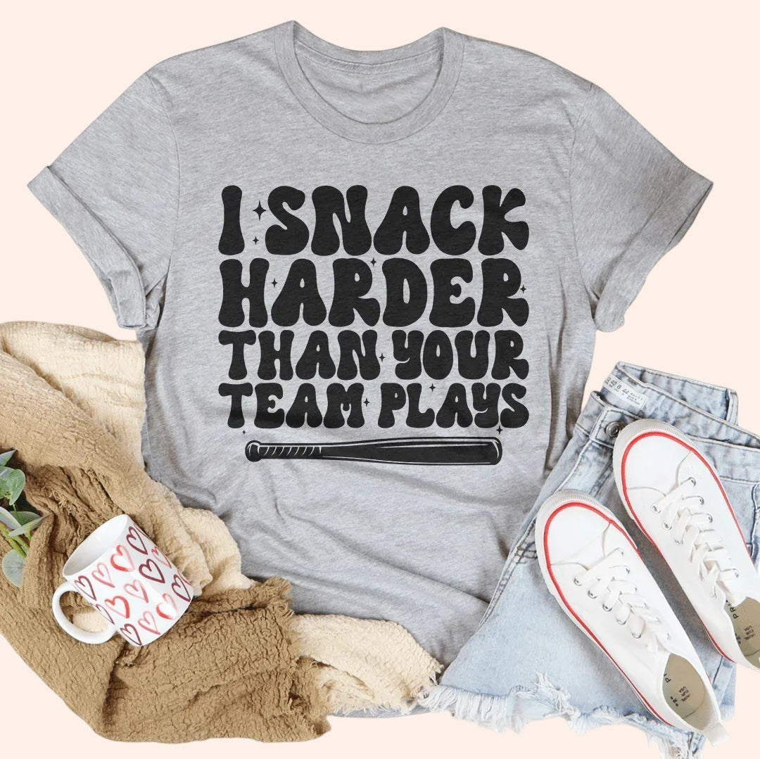 Bleacher Babe grey graphic tee with "I Snack Harder Than Your Team Plays" text and baseball bat graphic.