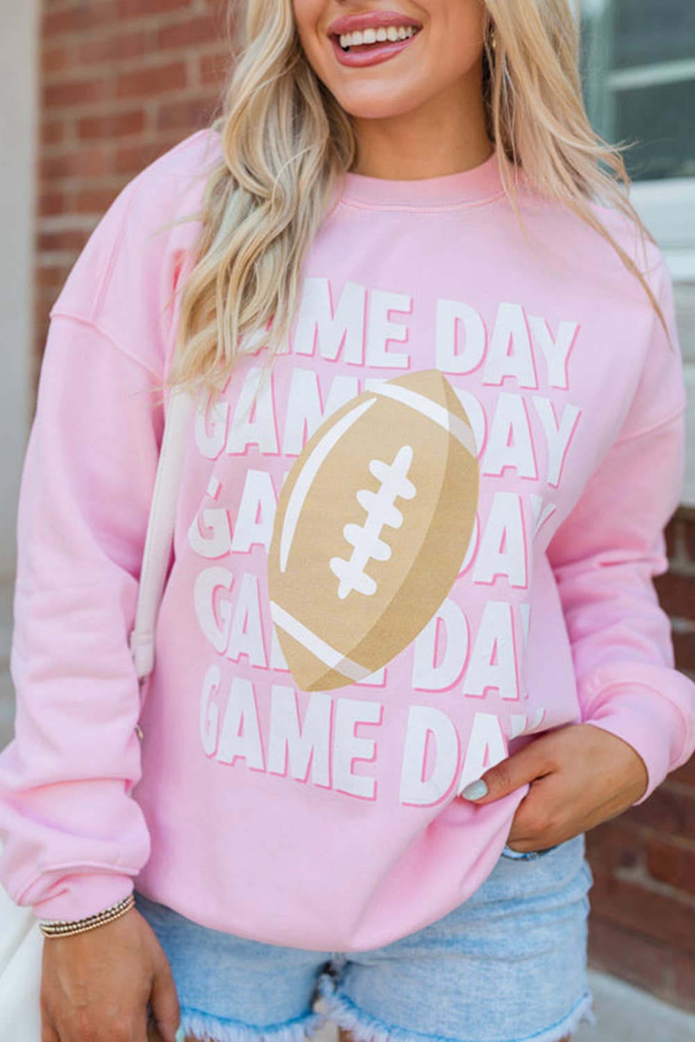 Woman wearing pink Game Day football sweatshirt with gold football graphic