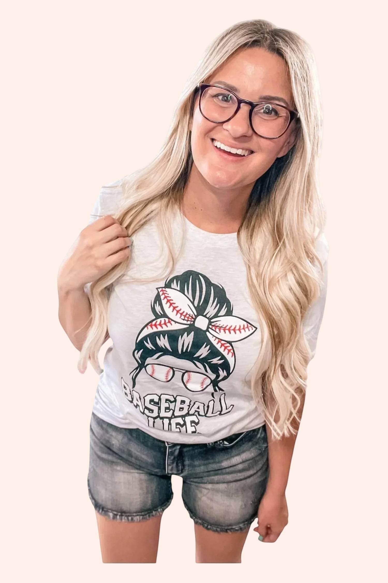 Bleacher Babe white graphic tee with baseball life messy bun design, short sleeves, and crew neck. Model wears glasses.