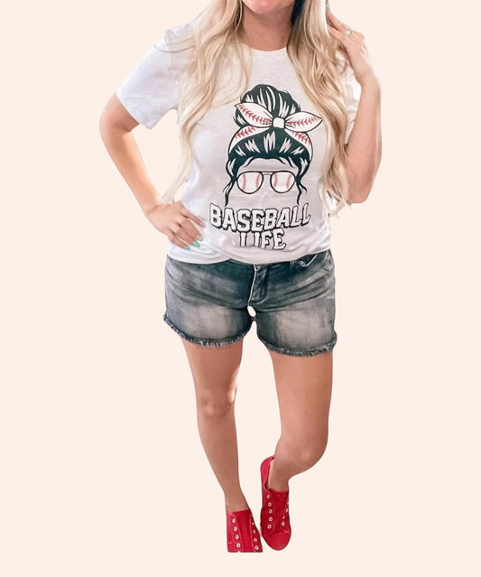 Bleacher Babe white graphic tee with baseball life design, featuring a messy bun with baseball stitches and sunglasses.