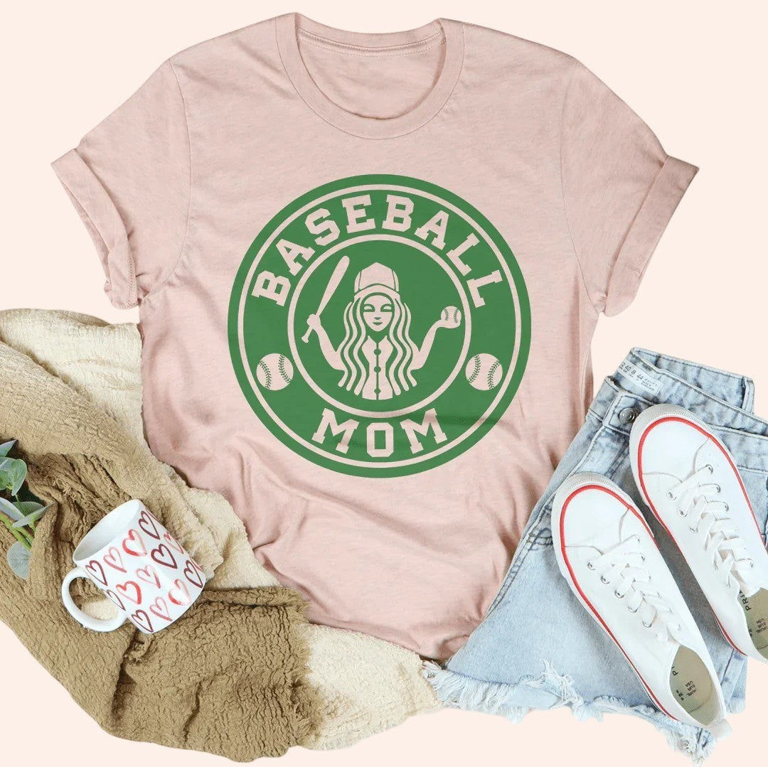 Bleacher Babe pink graphic tee with green "Baseball Mom" circular logo, featuring a woman with a baseball cap and bat.