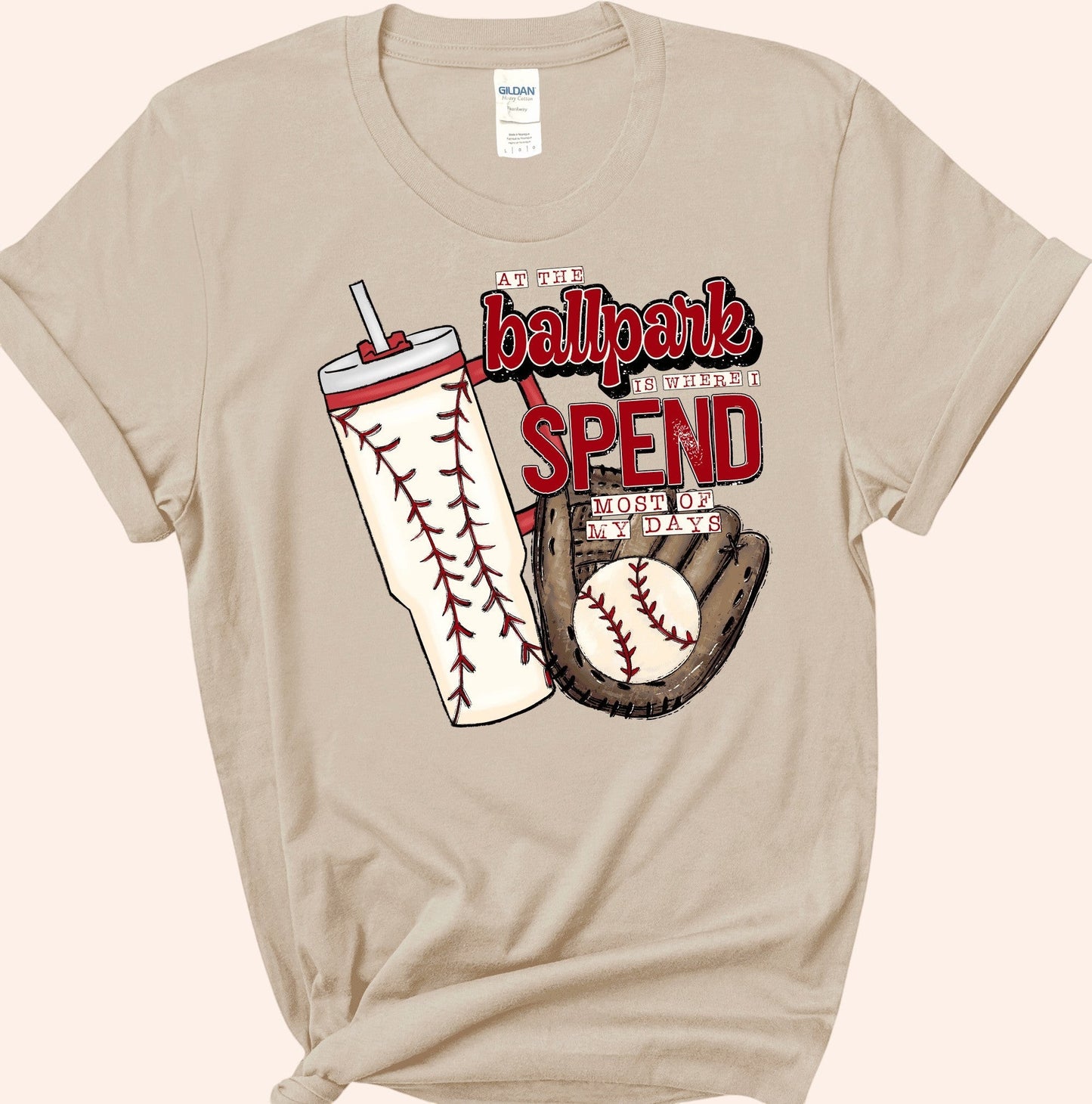 Bleacher Babe baseball mom graphic tee in tan, featuring a baseball glove, ball, and tumbler with baseball stitching.