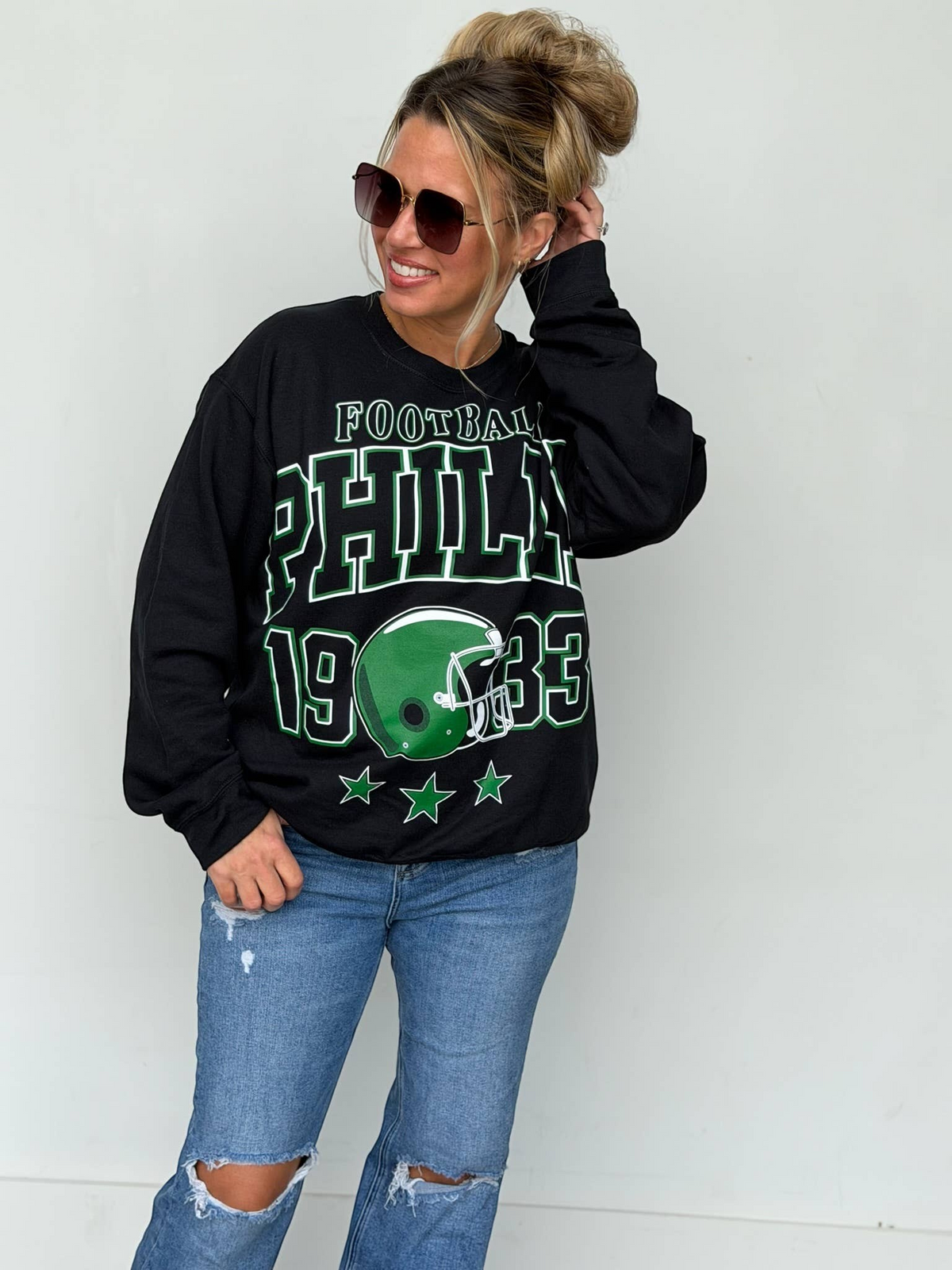 Bleacher Babe black unisex sweatshirt with vintage green Philly football screen print worn by a woman in sunglasses