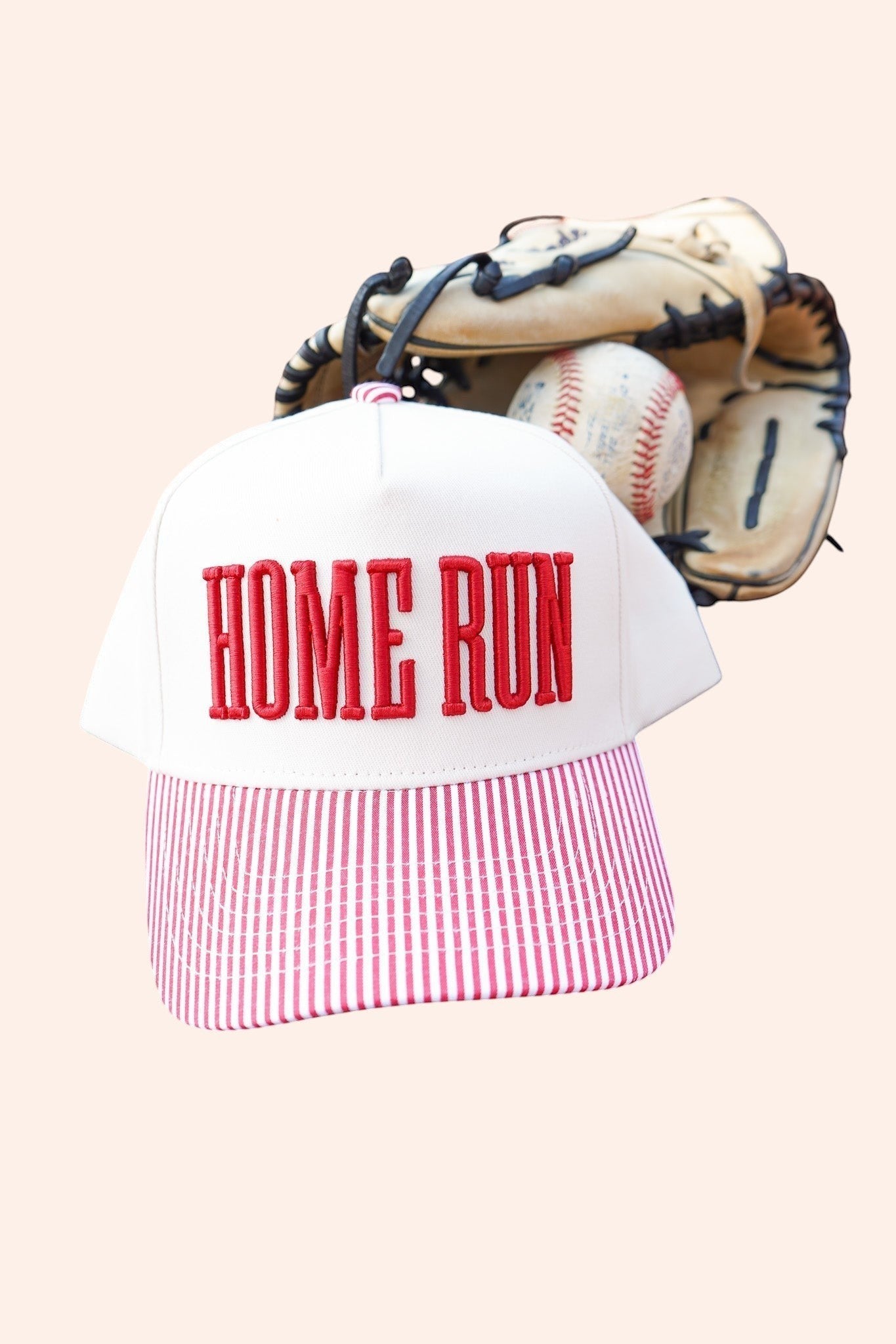 Bleacher Babe Homerun Trucker Hat with white crown, red embroidery, and red & white striped bill. Baseball glove and ball in background.