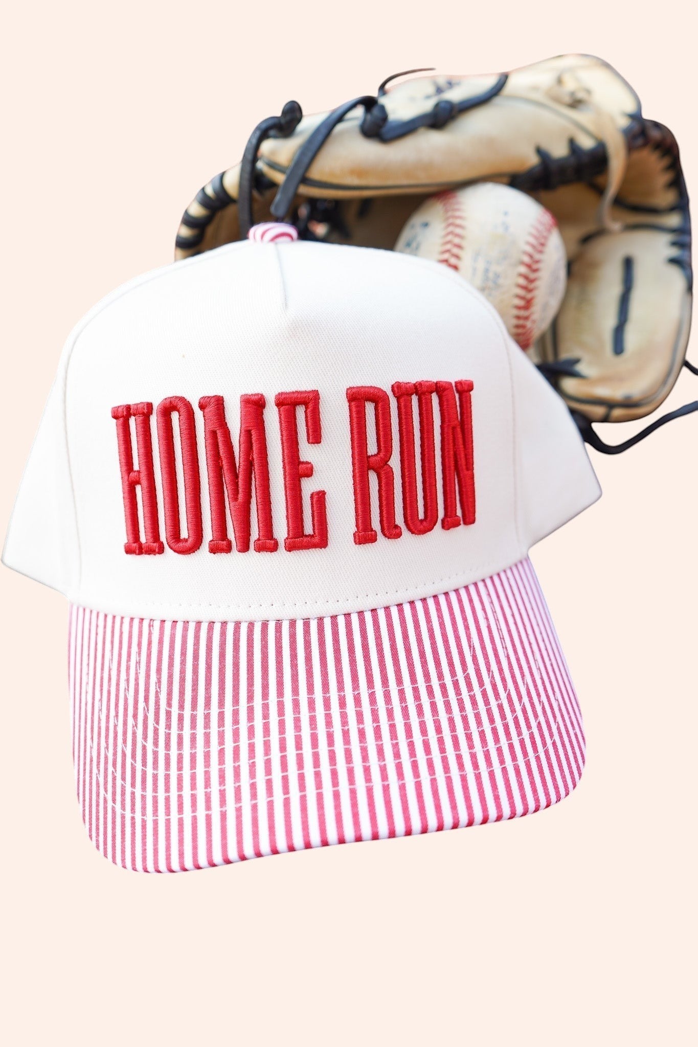 Bleacher Babe Homerun trucker hat with white front, red embroidery, and red and white striped bill. Baseball glove and ball in background.