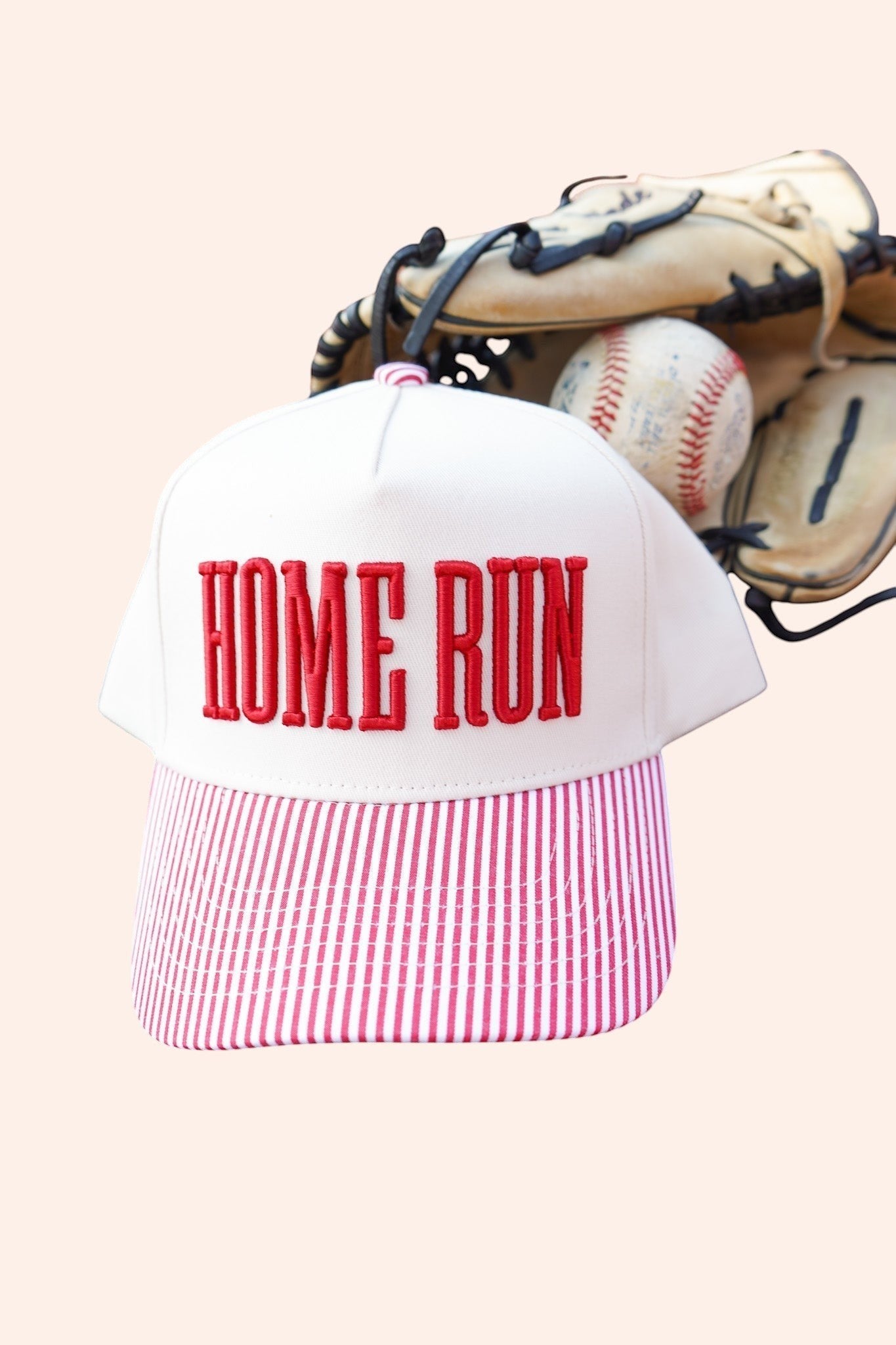 Bleacher Babe Homerun Trucker Hat with white front, red embroidery, and red striped bill. Baseball glove and ball in background.