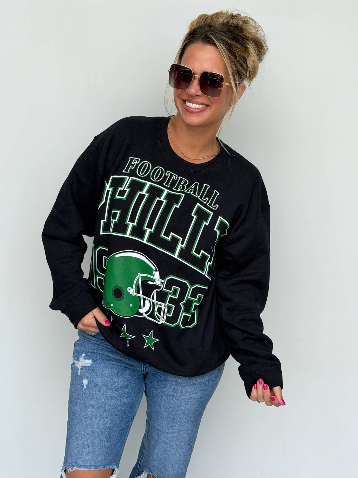 Bleacher Babe black unisex sweatshirt with green Philly football screen print worn by a woman in sunglasses