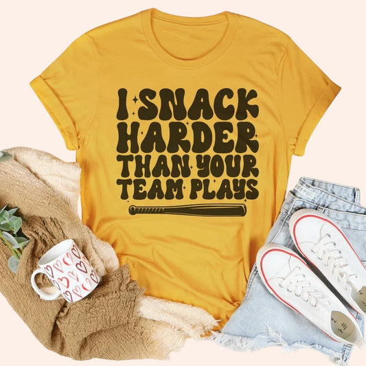 Bleacher Babe yellow graphic tee with "I Snack Harder Than Your Team Plays" text and baseball bat graphic.
